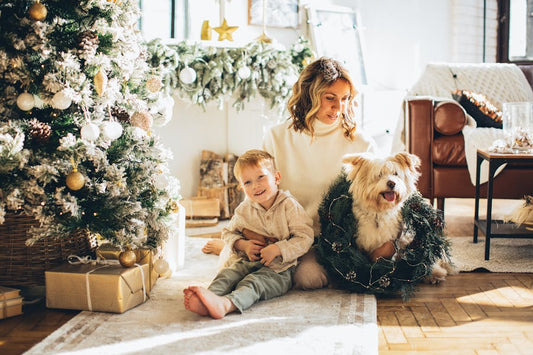 Mother, kid and a dog sitting by a decorated Christmas tree and wrapped presents.
