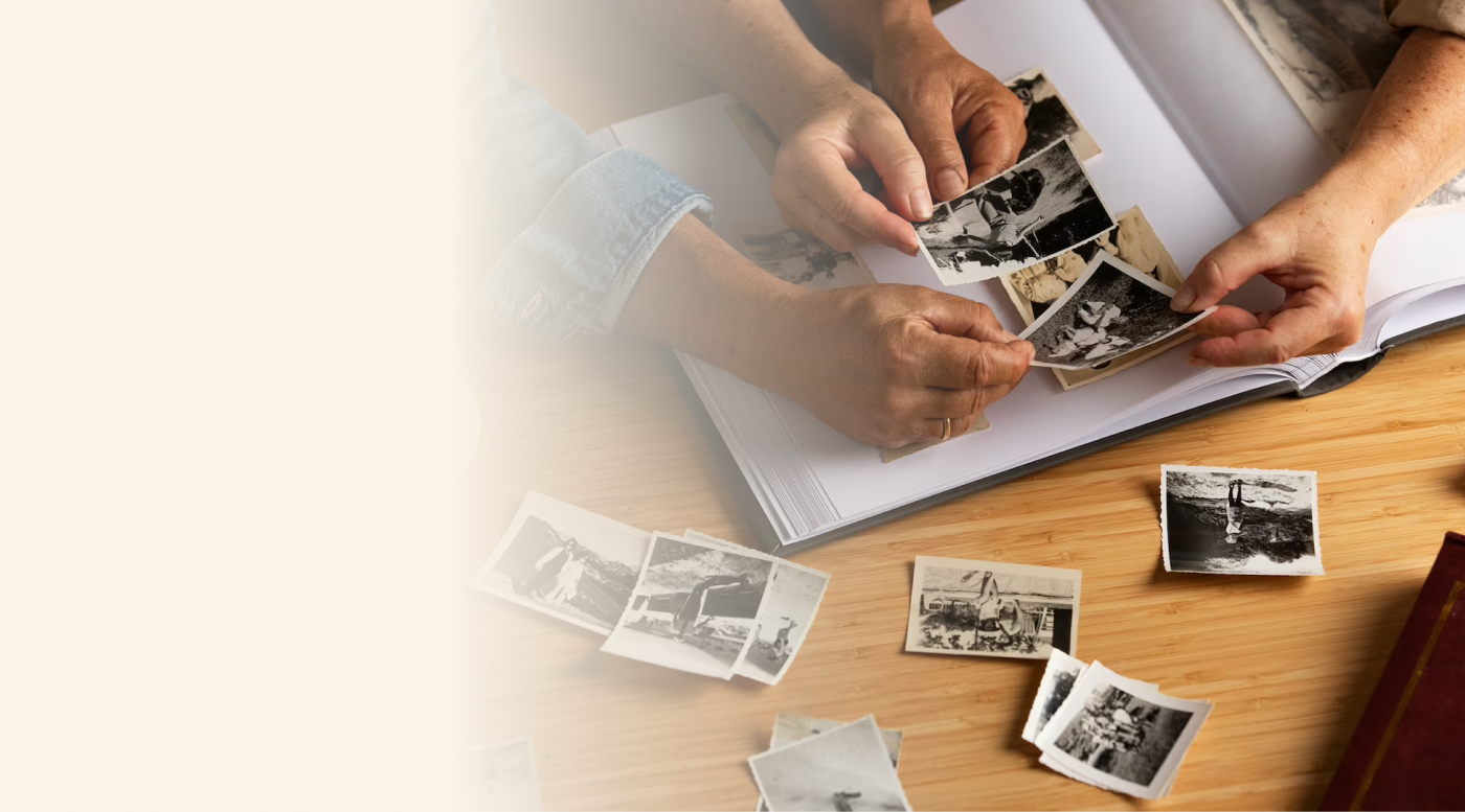Two hands sorting through vintage black and white photos, placing them into an album on a wooden surface