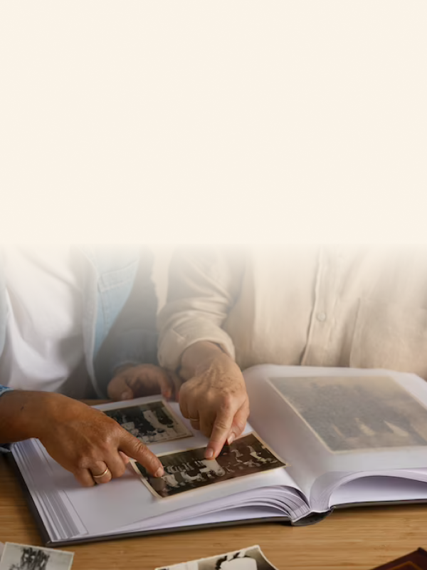 Two people sorting through vintage photos and placing them into an album on a wooden table.